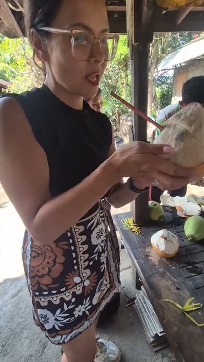 Cenny proeft een verse kokosnoot met rietje in de houten warung op de plantage