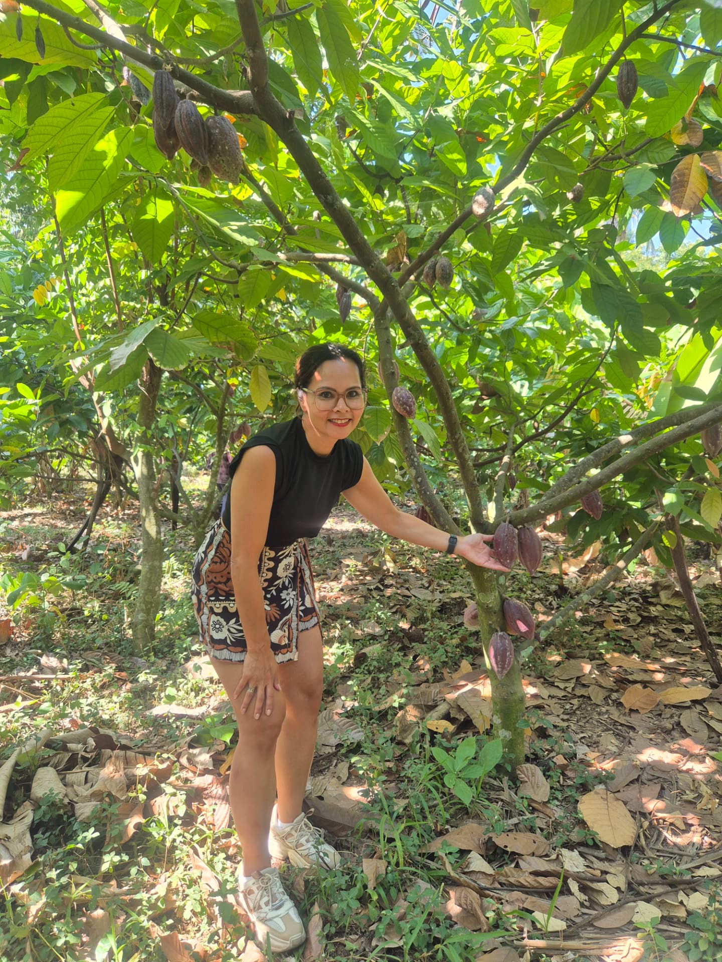 Cenny staat tussen de cacaobomen op de plantage in Jembrana, Bali, met rijpe cacaovruchten aan de tak