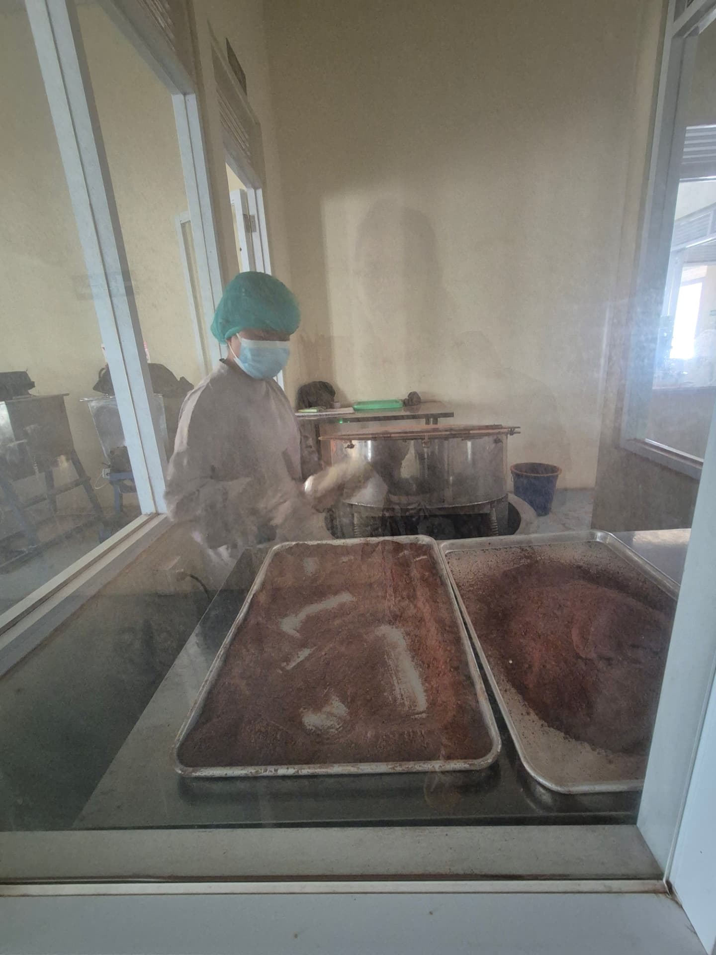 Medewerker verwerkt cacao op grote bakplaten in de cacaofabriek in Jembrana