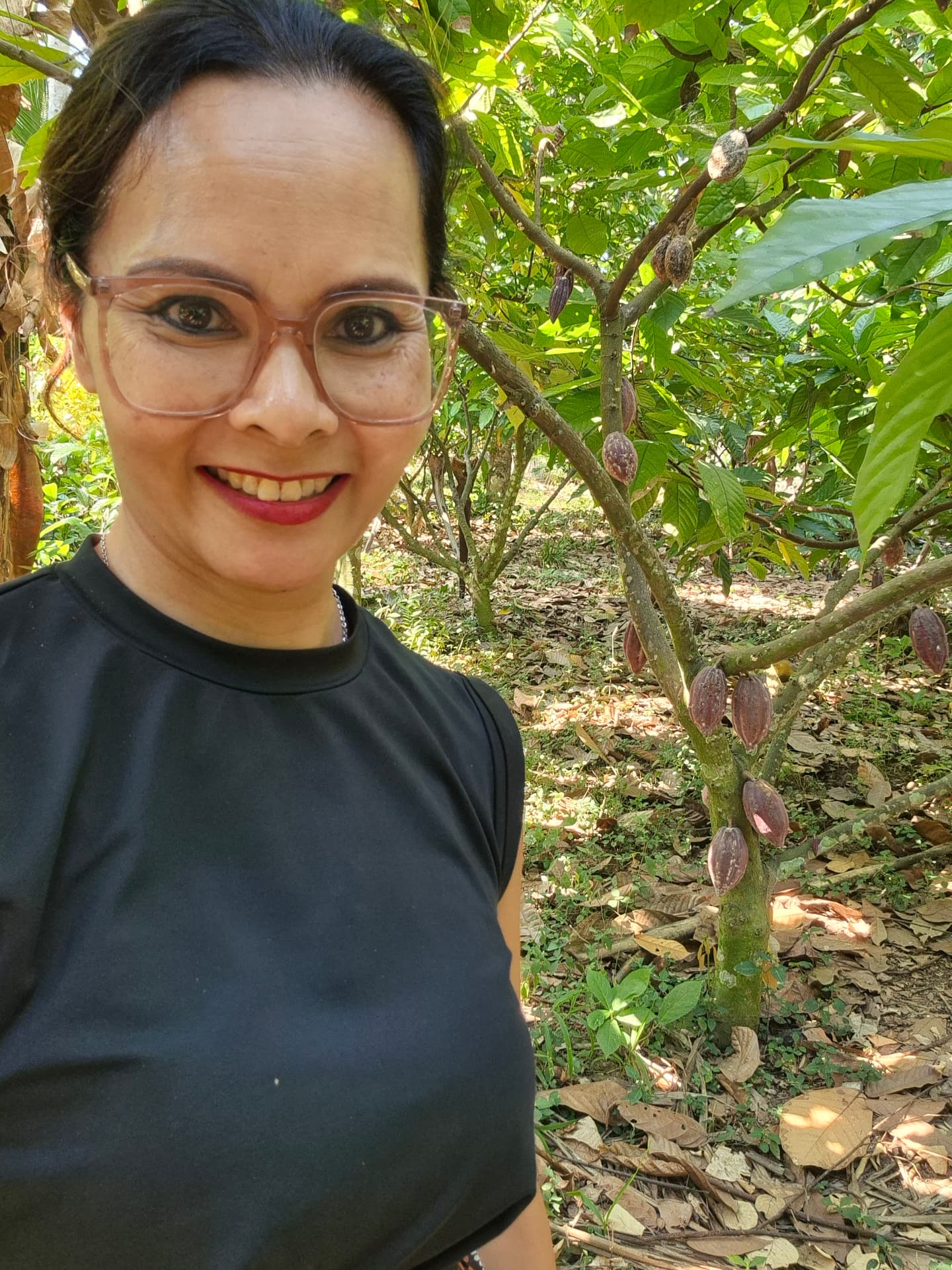 Cenny lachend op de cacaoplantage op Bali met een cacaoboom vol vruchten achter haar